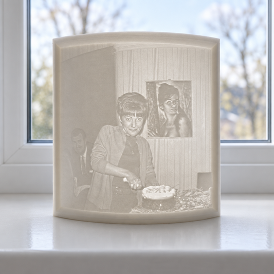 Curved white 12 × 12 cm lithophane panel standing on a window sill, with a portrait visible in natural daylight